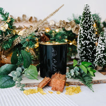 Load image into Gallery viewer, Green candle with a gold lid & MJM Home Fragrance branding. Surrounded by ingredients that depict the scent notes such as wood, eucalyptus, pine and resin. All sitting in front of a festive background