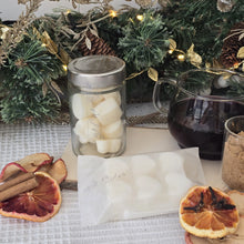 Load image into Gallery viewer, Jar & Bar of wax melts surrounded by ingredients to depict their scent including, glass mug with dark liquid, cinnamon sticks, and dried oranges on a textured surface with Christmas decorations.