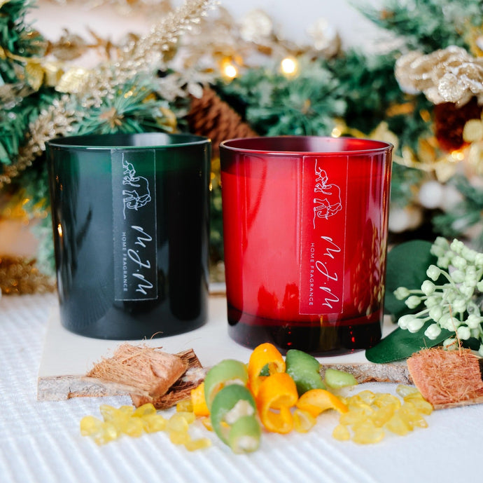 Two candles, one green and one red, on a table with decorative items to depict ingredients and a blurred Christmas tree in the background.