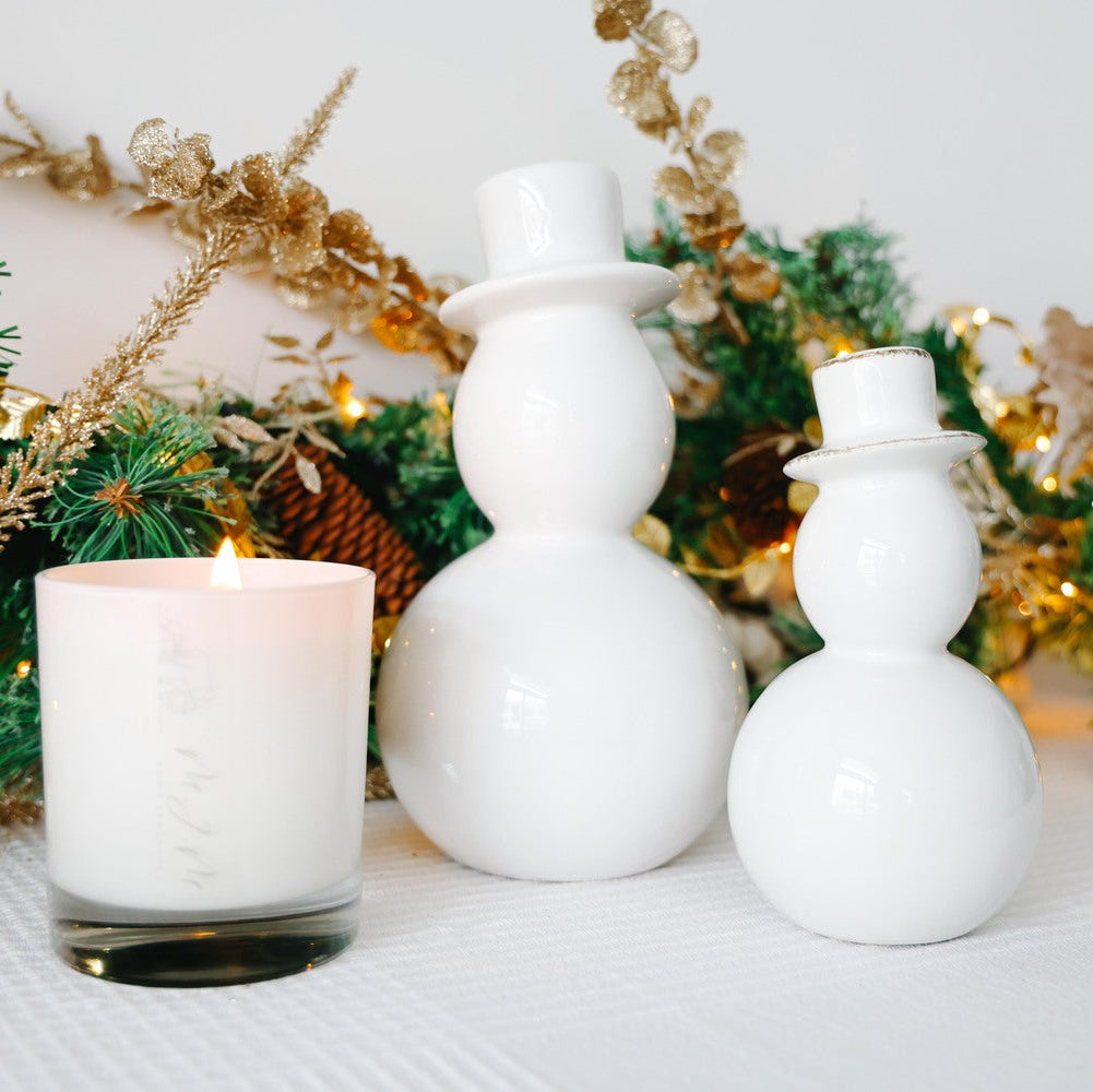 Two white ceramic snowman decorations with a lit candle on a decorative background.