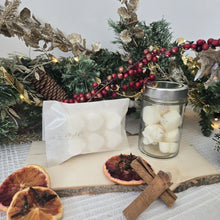 Load image into Gallery viewer, Decorative setup with wax melts, cinnamon sticks, and dried oranges in front of a Christmas wreath.
