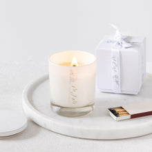 Load image into Gallery viewer, A picture of a medium lit candle in a white glass vessel, accompanied by a white gift box finished with MJM Home Fragrance branded ribbon
