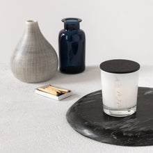 Load image into Gallery viewer, A lifestyle image of a small MJM Home Fragrance candle with a black lid
