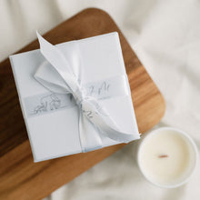 Load image into Gallery viewer, An image of a white gift box finished with MJM Home Fragrance branded ribbon, sitting next to a small wooden wick candle 
