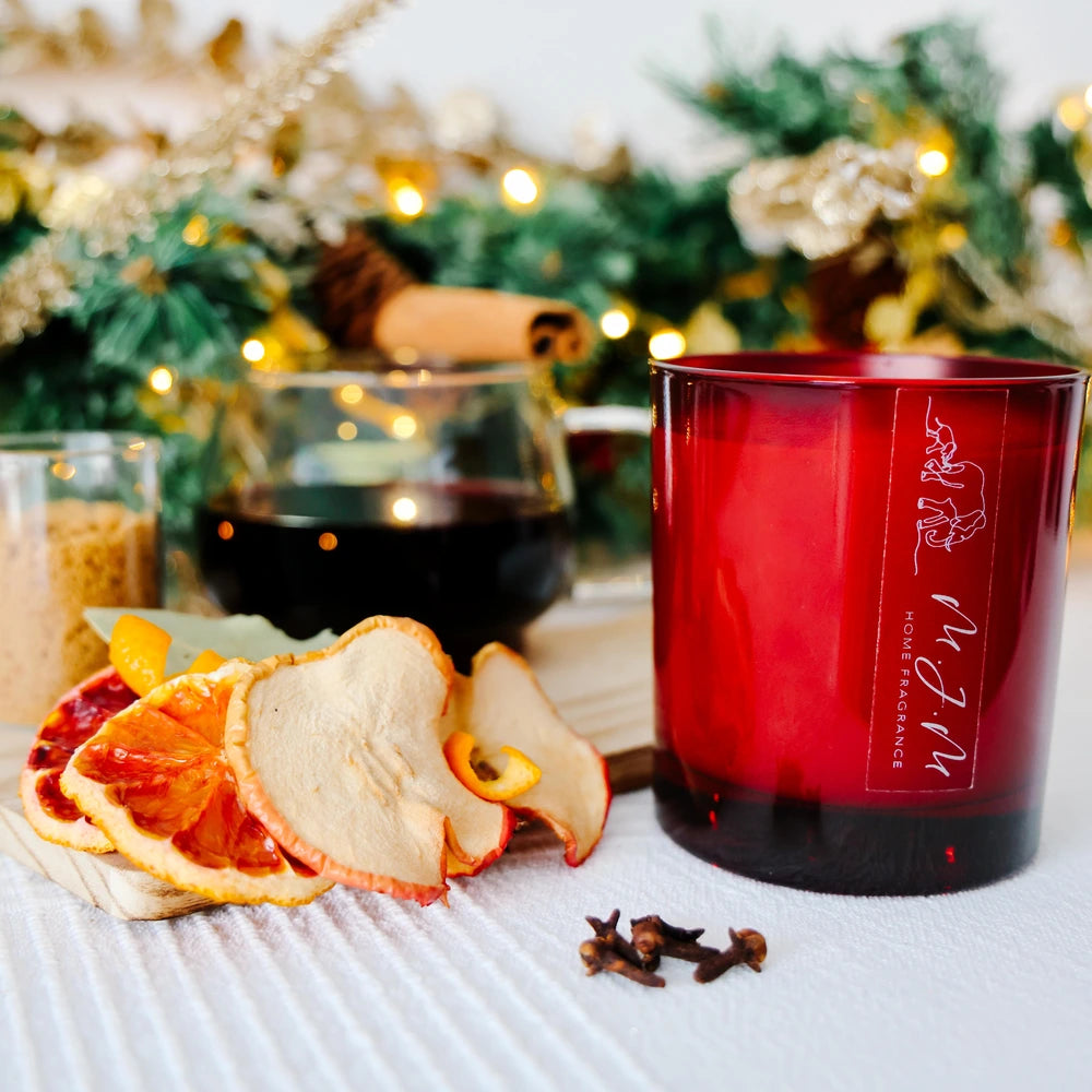 Red candle with brand name on a table with dried fruit and spices, Christmas decorations in the background